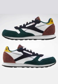 Sko med en blanding av hvitt mesh og grønn semsket skinn, med marineblå og burgunder detaljer, en svart gummisåle og Reebok-merke.