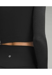 Schwarzes, langärmliges, eng anliegendes Oberteil mit gerippter Textur, kombiniert mit hoch taillierten schwarzen Leggings, die ein kleines Logo am hinteren Bund haben.