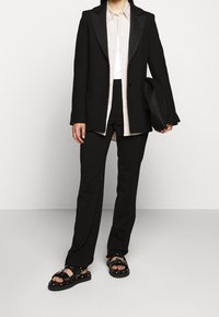 Mustat bleiserit, joissa on satiinikaulukset, yhdistettynä raitapaitaan ja mustiin muotoiltuihin housuihin. Korostettu paksuilla mustilla sandaaleilla, joissa on niittejä.