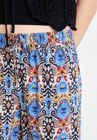 Pantaloni con motivo e vita con coulisse, caratterizzati da un design vivace in blu, rosso e oro su uno sfondo neutro, realizzati in tessuto leggero.