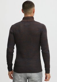 Dunkel gestrickter Rollkragenpullover mit einer Mischung aus braunen und navyblauen Farbtönen. Dünner, strukturierter Stoff mit eng anliegenden Ärmeln und unterem Saum.