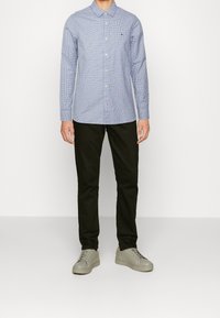 Camisa de manga larga de cuadros azul claro con cuello abotonado, combinada con pantalones negros y zapatillas grises. Diseño y ajuste simples.
