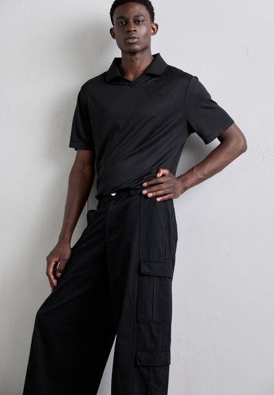 Svart polo skjorte med korte ermer og en subtil tekstur, parret med løse svarte cargo-bukser med sidelommer.