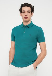 Πράσινο μπλουζάκι πόλο με πλάκα δύο κουμπιών, κοντά μανίκια και μικρό λογότυπο στο στήθος. Κατασκευασμένο από απαλό, υφασμάτινο μείγμα βαμβακιού με υφή.