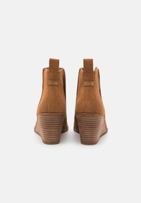 Bottines en daim marron à talon compensé, avec une semelle texturée et des rayures verticales marquées, agrémentées d'une languette de tirage et d'un logo.