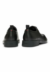 Scarpe in pelle nera con profilo basso, punta rotonda e suole in gomma testurizzata. Presentano un tappo ad anello e un sottile logo del marchio sul tallone.