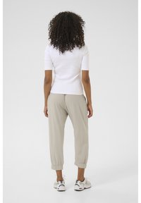 White fitted short-sleeve top paired with light beige tapered pants. Pants have elastic cuffs; model wears white and navy sneakers.