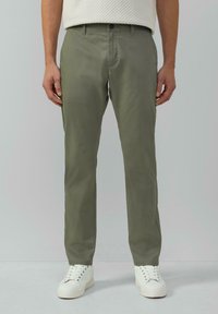 Hellolivgrüne Chinos aus glattem Stoff, mit geradem Bein, Seitentaschen und Knopfverschluss, getragen mit weißen Sneakers.
