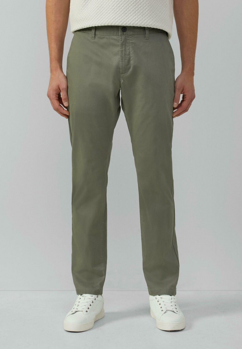 Hellolivgrüne Chinos aus glattem Stoff, mit geradem Bein, Seitentaschen und Knopfverschluss, getragen mit weißen Sneakers.