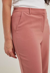 Skräddarsydda rosa byxor med en slät yta, utrustade med sidofickor och en slim fit-design. Platt front med en subtil veckdetalj.
