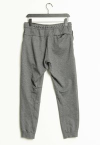 Grå sweatpants med elastisk midjeband och muddar, hängande på en svart galge mot en vit bakgrund.