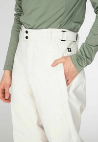 Witte sneeuwbroeken met een rechte snit, twee zwarte knopen en een riem. Opvallende zakdetails aan de zijkant en een textuur die geschikt is voor winterkleding.