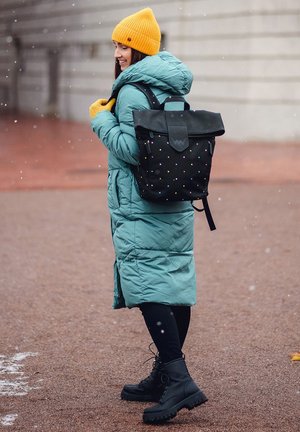 Green puffer coat, black backpack with colorful dots, yellow knit beanie, black lace-up combat boots, black leggings. Snow falling in background.