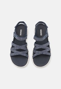 Sandali blu marino con più cinturini incrociati, tessuto strutturato e una cinghia alla caviglia regolabile. Presentano una suola scura e imbottita.