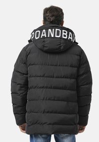 Schwarze Steppjacke mit Kapuze und weißer Beschriftung "POANDBAR". Das Design umfasst gesteppten Abschnitte zur Isolierung und eine glatte, matte Oberfläche.