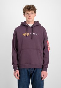 Fialová mikina s predným vreckom, kapucňou so šnúrkou a logom "Alpha Industries". Obsahuje rebrované manžety a červenú nášivku na rukáve.