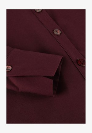 Bordeaux knoopshirt met een puntige kraag, voorzien van ronde bruine knopen en een gestructureerde stof. Opgevouwen manchet zichtbaar aan de linkerkant.