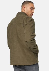 Olijfgroen corduroy jasje met een kraag, knoopsluiting bij de cuffs en een gestructureerd oppervlak, met een achterstuk detail.