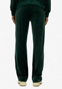 Fluwelen groene sweatpants met een losse pasvorm, elastische tailleband en rechte benen. Ontworpen voor comfort met een gladde textuur en een subtiele glans.
