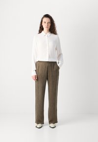 Witte blouse met lange mouwen en knopen, met een gestructureerd oppervlak, gecombineerd met bruine pantalon met een subtiel luipaardpatroon.