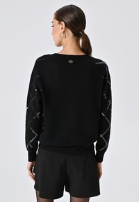 Maglione nero con design testurizzato, dettagli argentati sulle maniche, orlo a coste e scollo arrotondato.