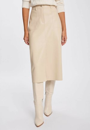 Gonna midi beige a vita alta con tasche frontali, abbinata a stivali beige al ginocchio con punta a punta, indossata con un maglione color crema.