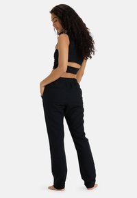 Black cropped top with cut-out back paired with loose-fitting black pants featuring pockets and subtle hardware detail, set against a neutral background.
