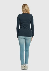 Mørkeblå langermet ribbestrikket skjorte, båret med lyseblå trange jeans og grå joggesko, sett bakfra.