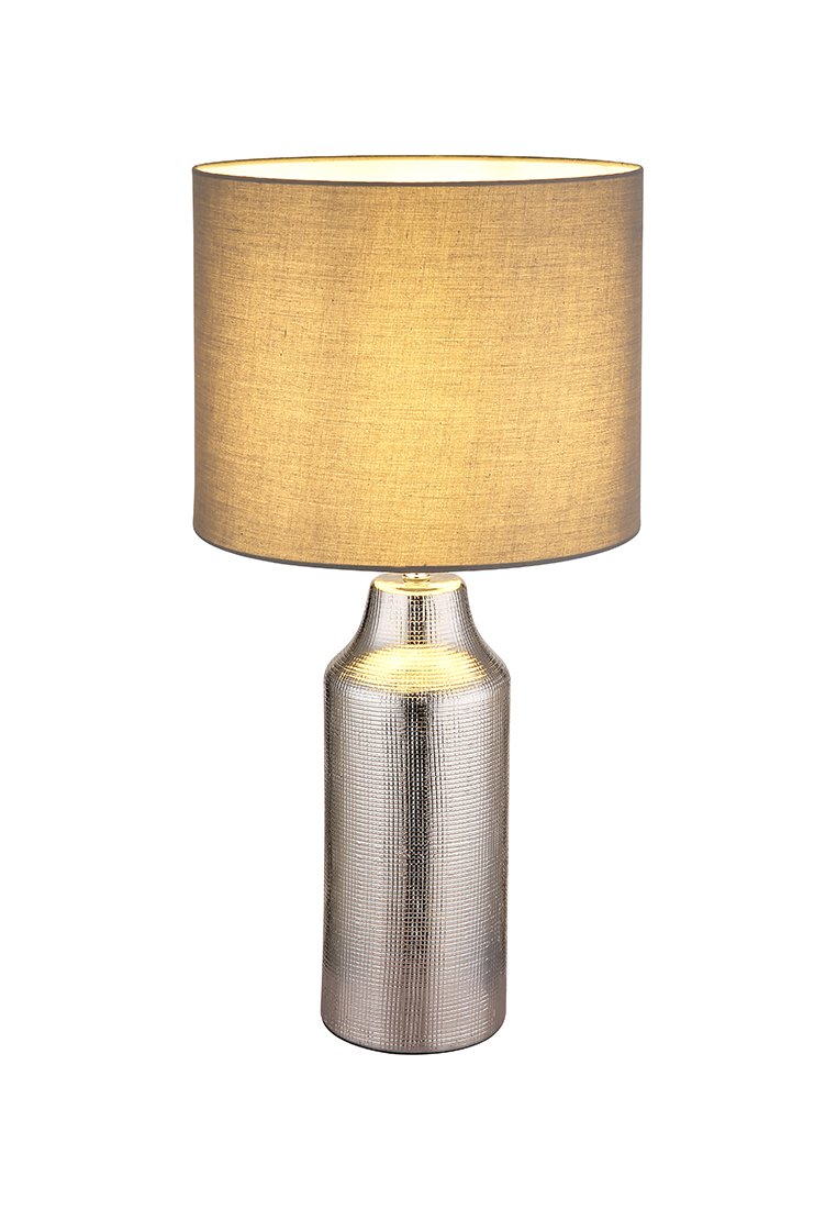Stolní lampa se stříbrnou texturovanou keramickou základnou a válcovým béžovým textilním stínidlem. Stínidlo je jemně osvětlené zevnitř.