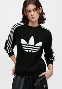 Sweater de malha preto com tecido texturizado, apresentando um grande logo trefoil branco da Adidas na frente e três riscas brancas nas mangas.