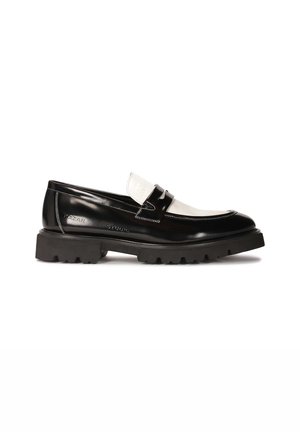 Black patent leather loafers with a white leather accent, thick black rubber tread sole, and stitched detailing. Smooth texture with a shiny finish.