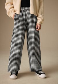 Schwarz-weiß karierte Hose mit weitem Bein und elastischem Bund, mit weitem Schnitt und fließendem Stoff. Kombiniert mit schwarzen Turnschuhen.