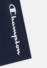 Shorts navy en tissu mélangé de coton, arborant un logo "Champion" blanc sur le côté, avec une texture lisse et une coupe droite.