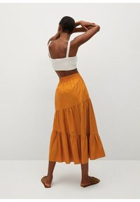 Gonna midi a balze in misto cotone color giallo senape con vita elastica arricciata. Indossata con un top bianco attillato e sandali bassi.