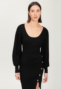 Zwarte geribde jurk met een ronde halslijn, lange pofmouwen en zijknopen. Heeft een hoge split tot boven de dij voor extra detail.