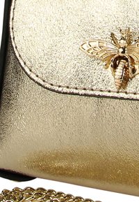 Goldfarbene metallische Handtasche mit strukturiertem Finish, gerundetem Klappdeckel und einem bienenförmigen Akzent. Verfügt über einen goldenen Kettenriemen zum Tragen.