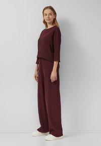 Bordeaux gebreid outfit met een driekwart mouw top en wijd uitlopende broek. Soepele textuur met een relaxte pasvorm, gecombineerd met witte sneakers.