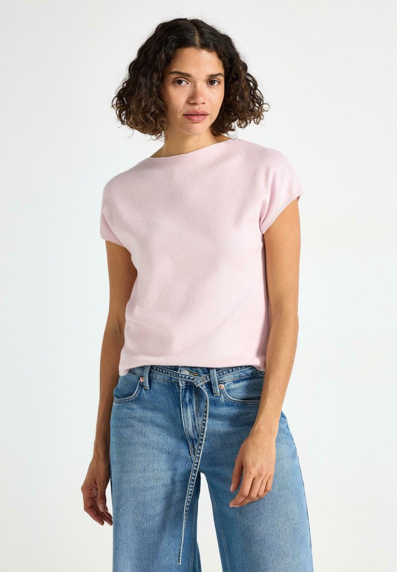 Ljusrosa kortärmad topp med rund halsringning, tillverkad av mjukt material, matchad med blå vida jeans i denim. Slät textur, enkel design.