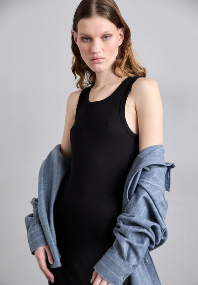 Čierne bezrukávové šaty s priliehavým strihom, skombinované s svetlomodrou oversized košeľou s gombíkmi, ktorá má károvaný vzor.