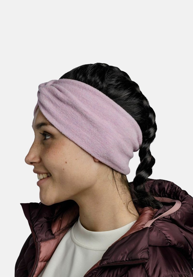Pink fleece headband with a twist design, soft texture, and smooth finish. Worn over dark, braided hair and paired with a puffy jacket.