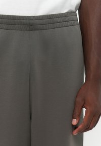 Grå tapered bukser med elastisk talje, lavet af glat stof. Teksturen er blød, og designet har en minimalistisk æstetik.