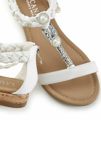 Witte sandaal met gevlochten stoffen band, parelaccenten, zilveren hardware en kurken zool. Glad oppervlak met stiksels.