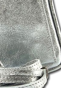 Metallisch zilveren handtas met een gestructureerde afwerking, voorzien van een dunne schouderband en een schoon, hoekig ontwerp. Stitchingdetails versterken de structuur.