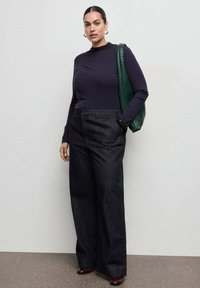 Haut bleu marine à manches longues associé à un pantalon en jean foncé taille haute, à jambes larges. Accessoirisé d'un sac cabas vert texturé et de chaussures bordeaux.