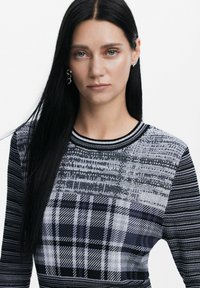 Maglione a maglia con un motivo a quadri bianco e nero e diverse trame. Collo rotondo e maniche lunghe con accenti a righe.