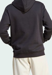 Svart hoodie med mjuk textur, med en känguruficka och ribbad fåll. Bärs över krämfärgade, löst sittande byxor.