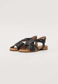 Black leather sandals with crisscross straps, open toe, and a small block heel. Adjustable buckle detail for fit. Warm-toned sole.