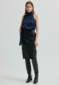 Top senza maniche di satin blu navy con collo drappeggiato; gonna a tubo nera in pelle; stivali con tacco al ginocchio neri. Design semplice e elegante con linee pulite.