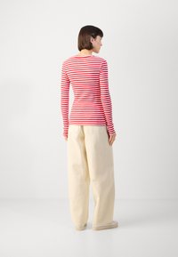 Red and white striped long-sleeve top, fitted at the waist, paired with loose, beige wide-leg pants and white shoes. Plain background.