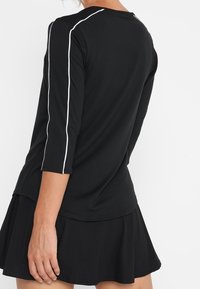 Schwarzes Langarmoberteil mit weißen Seitenstreifen, Rundhalsausschnitt und lässiger Passform, kombiniert mit einem schwarzen plissierten Rock.